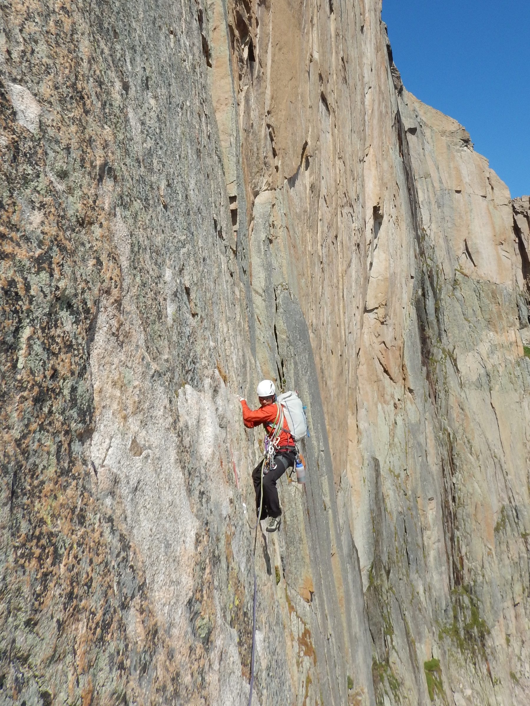 Jay climbing a steep granite wall beneath a clear blue sky